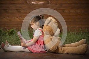 Little girl reading a book to her teddy bear