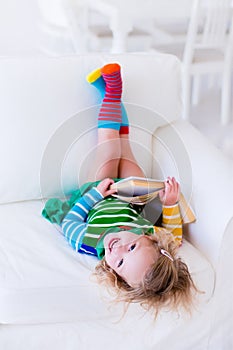 Little girl reading a book on a white couch