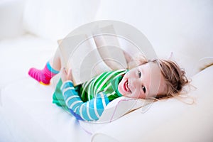 Little girl reading a book on a white couch