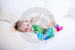 Little girl reading a book on a white couch