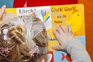 Little girl reading colourful book - Translation: Kikeriki, Gluck Gluck like the chicken photo