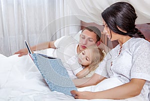 Little girl reading with her parents in bed