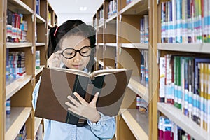 Little girl reading a textbook in the library