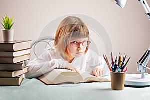 The little girl reads the book attentively. The first grader is doing her homework