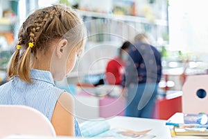 Little girl reads book with fairy tales in children`s library. Special reading kids room. Many shelves with bright interesting,