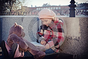 Little girl reads the book to a toy bear