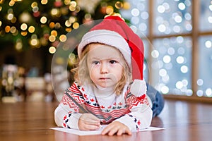 Little girl in a red Christmas hat writing a letter to Santa Claus