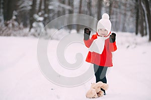Little girl in red coat with a teddy bear having fun on winter day. girl playing in the snow