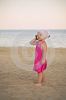 A little girl in a red dress is talking on the phone on the sea beach