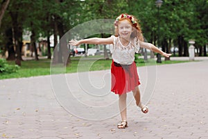 Little girl with red hair depicts bird in green summer p