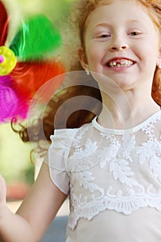 Little girl with red hair smiles and holds windmill
