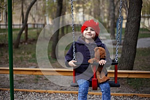 Little girl with red hat on the teeter-totter with her teddy bear