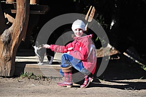 Little girl in a red jacket stroking a cat