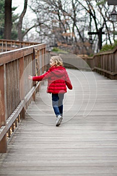 A little girl in a red jacket walks down the road touching the fence