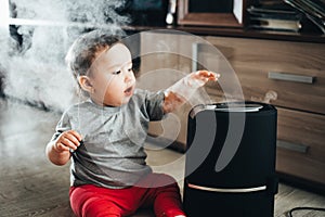 A little girl in red pants looks and touches the humidifier. Moisture in the house concept photo