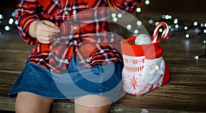 A little girl in a red plaid shirt and a denim blue skirt, opens the sweets from her Christmas gif