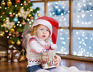 Little girl in red santa hat opening Christmas gifts