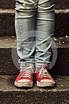 Little girl in red sneakers and jeans standing on the stairs