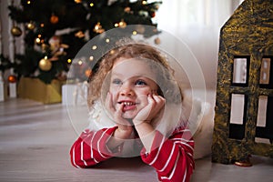 Little girl in red sweater lie under the Christmas tree and wait for a miracle