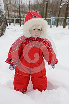 Little girl in a red winter jumpsuit plays with snow