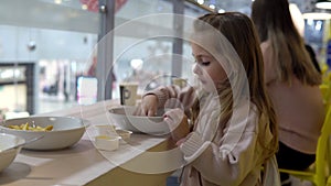 A little girl in a restaurant eats French fry with sauce. The child eats in the institution.