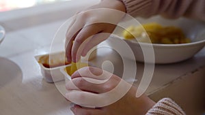 A little girl in a restaurant eats French fry with sauce. The child eats in the institution. Close-up of dipping