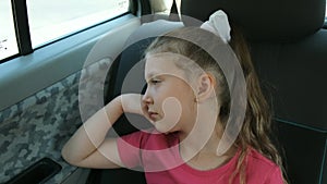 A little girl rides in the car, looking out the window. Outside the window flashed the trees and houses of the city