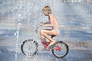 Little girl rides his bike among fountains