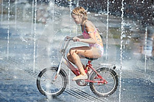 Little girl rides his bike among fountains