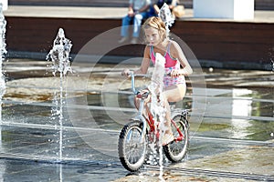 Little girl rides his bike among fountains