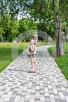 A little girl rides a scooter on a path in a Park on a Sunny summer day.