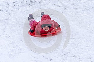 A little girl rides a sled from a winter slide