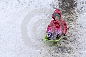 A little girl rides a sled from a winter slide