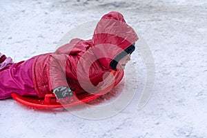 A little girl rides a sled from a winter slide