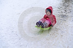 A little girl rides a sled from a winter slide