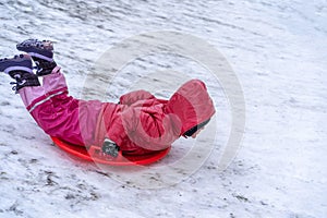 A little girl rides a sled from a winter slide