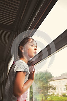 A little girl rides on a train and looks out the open window.