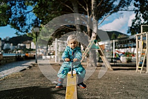 Little girl rides on a wooden swing-balancer holding the handle
