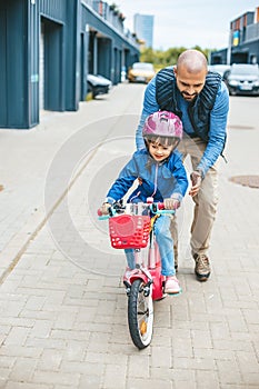 Little girl riding a bike with her father\'s hepl. Father teaching his little daughter to ride a bike