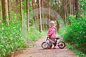 Little girl riding bike in summer forest