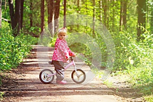 Little girl riding bike in summer forest