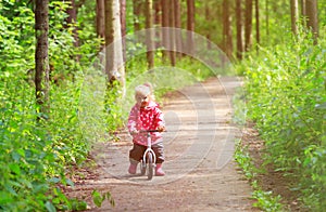 Little girl riding bike in summer forest