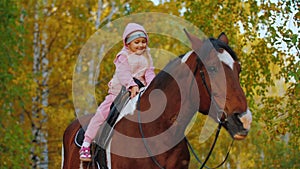 Little girl riding on horse hugging her and stroking, child sits on horse