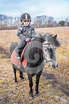 Little girl riding a little horse or pony in the winter in field in the winter