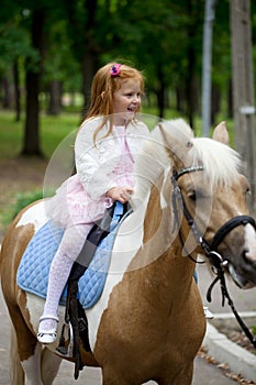 Little girl riding on a pony in a city park