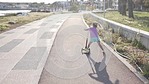 Little girl riding a scooter in the park by the sea.