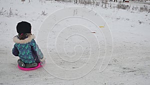 Little girl riding on snow slides rolling down the hills, in winter time winter holidays