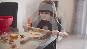 Little girl rolls out dough and helps her mother