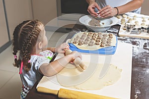 Little girl rolls out the dough, while her mother sculpts the dumplings for the holiday photo