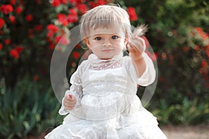 Little girl in rose garden next to a big bush of red roses